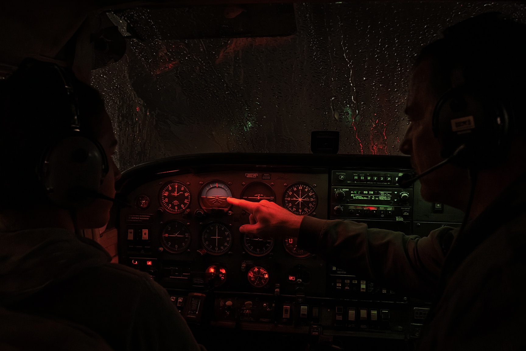 Night dual instruction in a trainer cockpit, rain on the windshield, instrument glow
