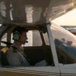 Student pilot in aviation uniform inside Cessna 172 during sunset, overlooking airport ramp.